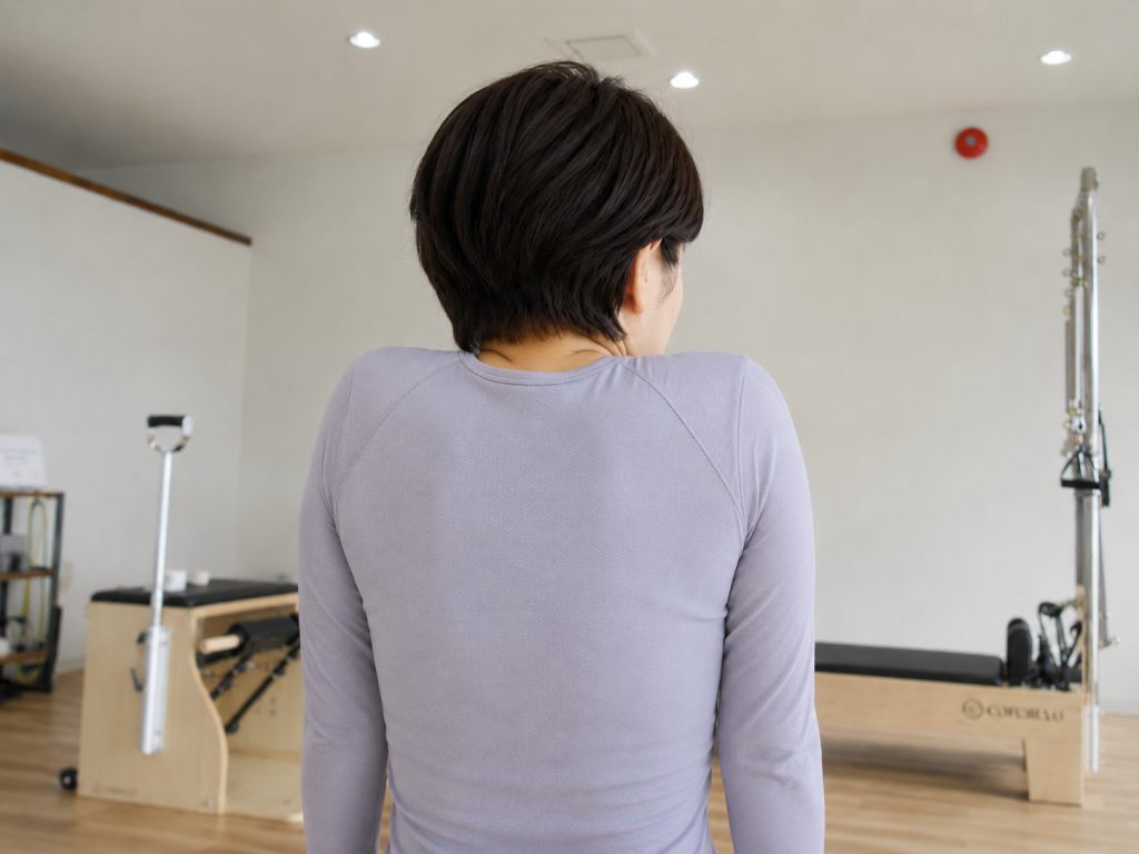 肩がすくみ、肩と耳の距離が近くなっている女性の後ろ姿