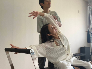 マシンピラティスでマーメイドをする女性に補助を入れているトレーナー