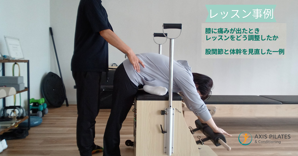 ピラティスマシンで殿筋ストレッチを行う女性を、トレーナーが骨盤に手を添えてサポートしている様子