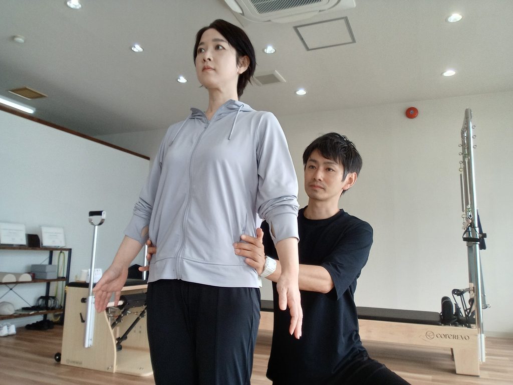 立った姿勢で、トレーナーが骨盤まわりに手を添え、身体の位置関係を確認しているAXISのレッスン風景。